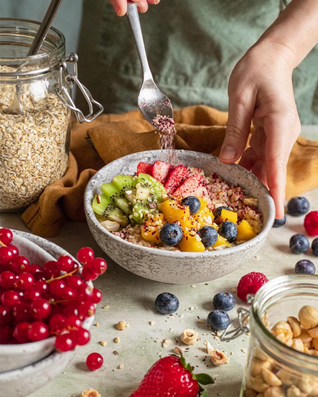 Das Foto zeigt, wie eine Hand geschickt "Food Finisher Porridge" über eine Schüssel mit Haferflocken und frischen Früchten streut, entsprechend dem Rezept für ein ausgewogenes Frühstück.