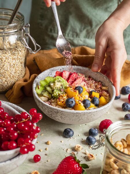 Das Foto zeigt, wie eine Hand geschickt "Food Finisher Porridge" über eine Schüssel mit Haferflocken und frischen Früchten streut, entsprechend dem Rezept für ein ausgewogenes Frühstück.
