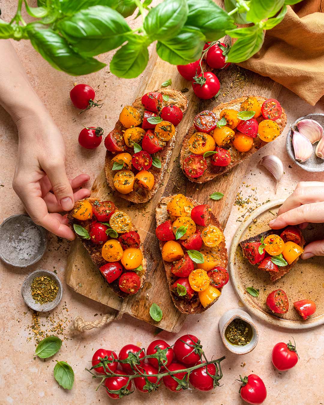 Das Foto zeigt rustikale Tomatenbruschettas, verfeinert mit "Food Finisher Tomaten Zauber" und frischem Basilikum, angerichtet auf einem Holzbrett nach Rezept.
