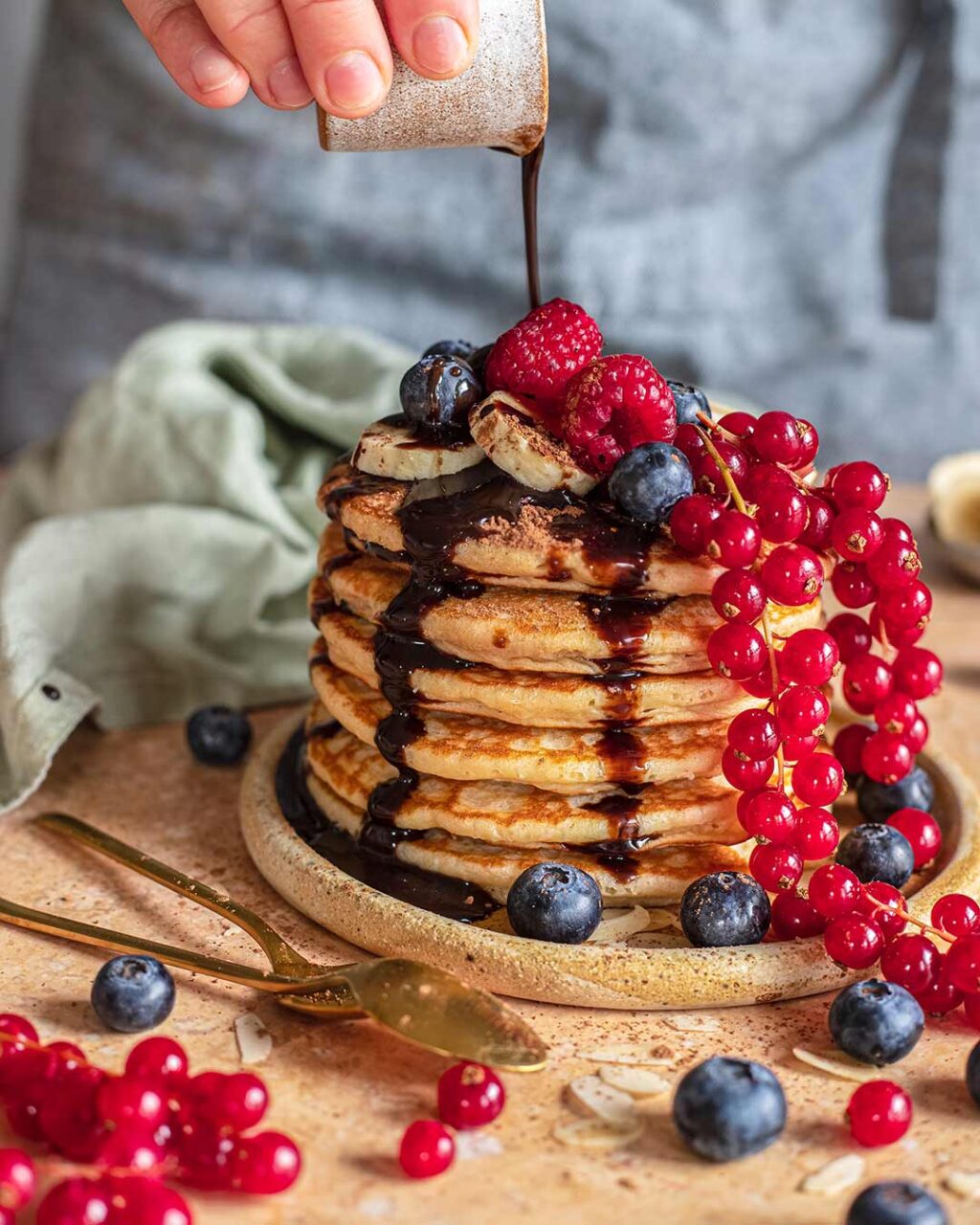 Stapel von Bananenpfannkuchen nach Rezept, übergossen mit Schokoladensoße und garniert mit frischen Beeren.