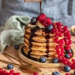 Stapel von Bananenpfannkuchen nach Rezept, übergossen mit Schokoladensoße und garniert mit frischen Beeren.