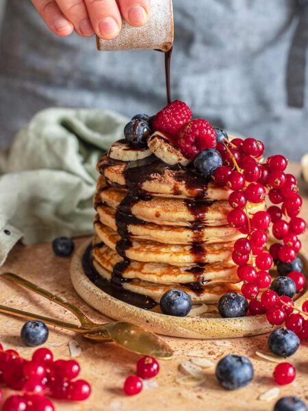 Stapel von Bananenpfannkuchen nach Rezept, übergossen mit Schokoladensoße und garniert mit frischen Beeren.