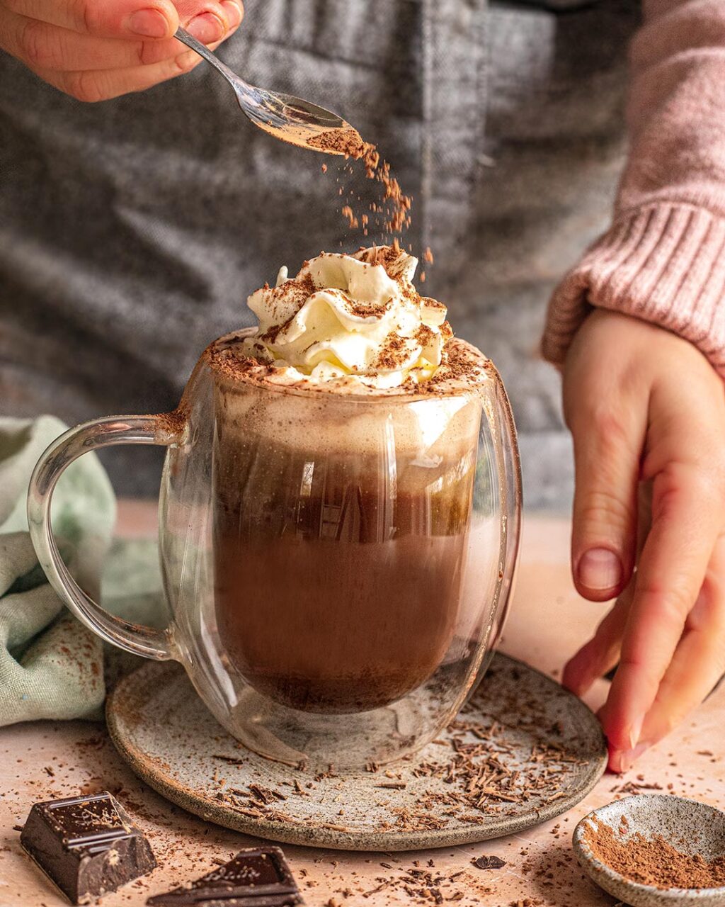 Das Foto zeigt heiße Kokosnuss-Schokolade nach Rezept, garniert mit Schlagsahne und Kakao, serviert in einer klaren Tasse.