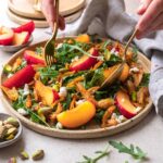 Bunter Salat mit Hähnchenfleisch, frischen Pfirsichen und Pistazien nach Rezept, sorgfältig angerichtet auf einem Keramikteller.