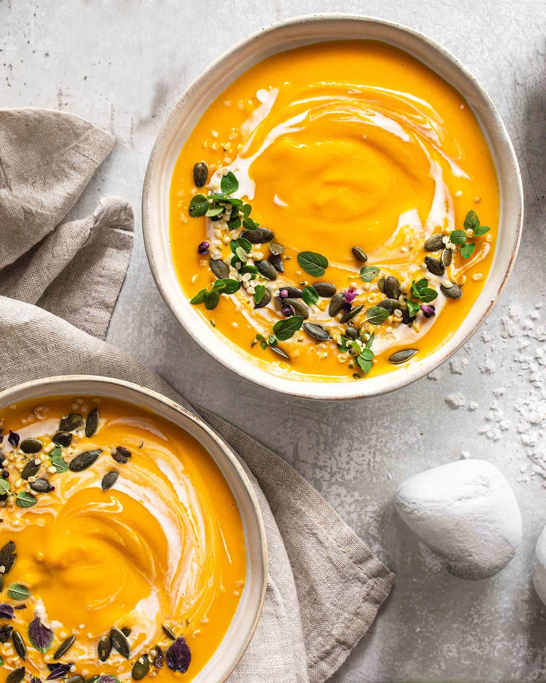 Das Foto zeigt eine cremige Kürbissuppe mit Ingwer und Kurkuma nach Rezept, verfeinert mit Kürbiskernen, BIO ASIA FOOD FINISHER und frischen Kräutern.