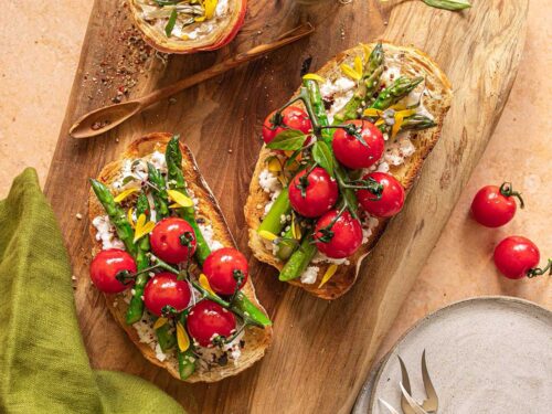 Das Foto zeigt zeigt köstliches Sauerteigtoast mit Ricotta, gegrilltem Spargel und Kirschtomaten nach Rezept, verfeinert mit BIO BRATEN FOOD FINISHER, präsentiert auf einem rustikalen Holzbrett.