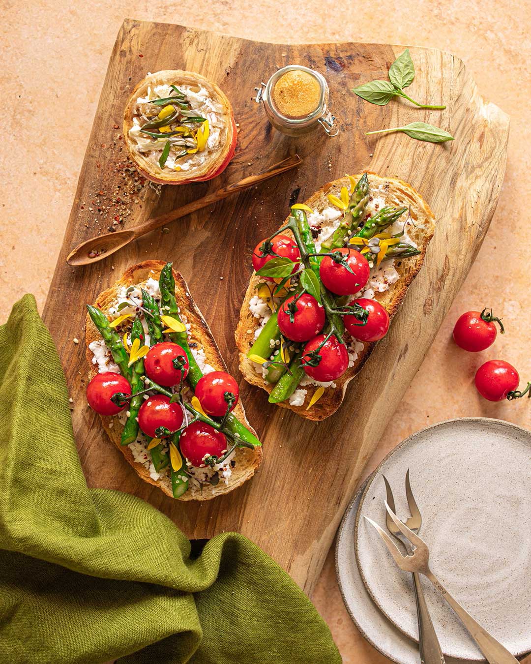 Das Foto zeigt zeigt köstliches Sauerteigtoast mit Ricotta, gegrilltem Spargel und Kirschtomaten nach Rezept, verfeinert mit BIO BRATEN FOOD FINISHER, präsentiert auf einem rustikalen Holzbrett.