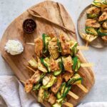 Vier Zitronen-Hähnchenspieße, kombiniert mit Artischocke und Zucchini, angerichtet auf einem rustikalen Holzbrett. Verfeinert mit dem Bio Braten Finisher von Luis Dias, der mit seiner Salz-Pfeffer-Mischung dem Gericht den letzten Schliff verleiht.