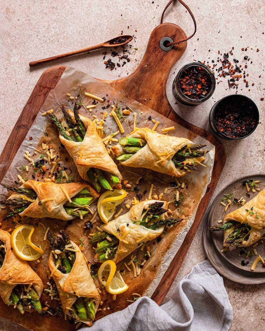 Kleine Spargel im Blätterteig Häppchen präsentiert auf einem Holzbrett. Gefüllt mit veganem Schinken und veganem Käse und verfeinert mit dem Bio Pommes de Terre Food Finisher von Luis Dias.