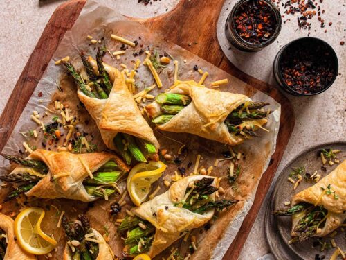 Kleine Spargel im Blätterteig Häppchen präsentiert auf einem Holzbrett. Gefüllt mit veganem Schinken und veganem Käse und verfeinert mit dem Bio Pommes de Terre Food Finisher von Luis Dias.