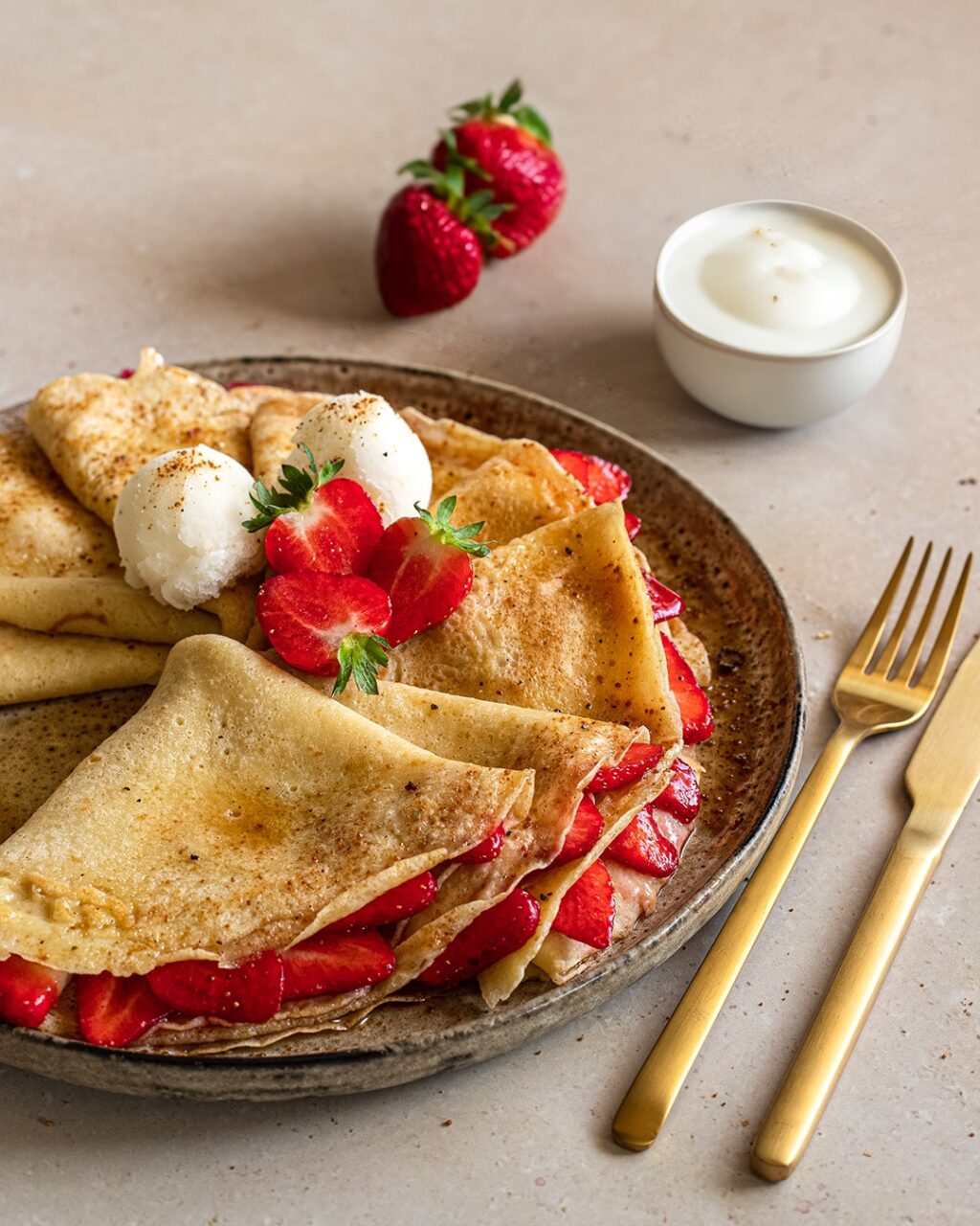 Erdbeer-Crêpes mit einer Füllung aus Erdbeeren, Vanilleschote und den Bio Food Finisher von Luis Dias. Schön angerichtet auf einem grauen Keramikteller mit halbierten Erdbeeren und zwei Kugeln feinem Vanilleeis.