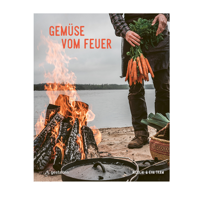 Das Foto zeigt ein Buchcover mit einem brennenden Lagerfeuer im Vordergrund und einer Person, die einen Bund Karotten hält. Der Titel des Buches "Gemüse vom Feuer" ist prominent abgebildet.