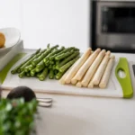 Grüner und weißer Spargel liegen frisch vorbereitet auf einem Schneidebrett in einer hellen Küche und symbolisieren saisonale, pflanzenbasierte Frühlingsküche.