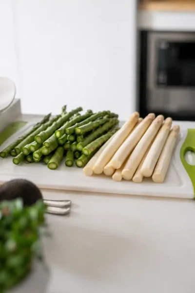 Grüner und weißer Spargel liegen frisch vorbereitet auf einem Schneidebrett in einer hellen Küche und symbolisieren saisonale, pflanzenbasierte Frühlingsküche.