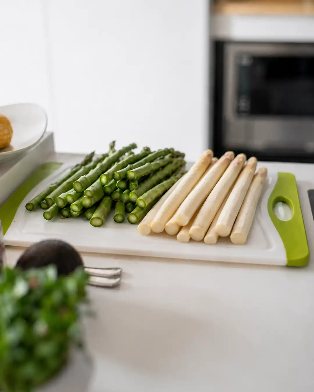 Grüner und weißer Spargel liegen frisch vorbereitet auf einem Schneidebrett in einer hellen Küche und symbolisieren saisonale, pflanzenbasierte Frühlingsküche.