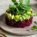 Ein kunstvoll angerichtetes veganes Tatar aus cremiger Avocado und aromatischer Rote Bete, verfeinert mit süßem Senf, Zitronensaft, roten Zwiebeln und Knoblauch. Abgerundet mit dem Bio Lecker-Ei Food Finisher von Luis Dias – perfekt als leichte Vorspeise.