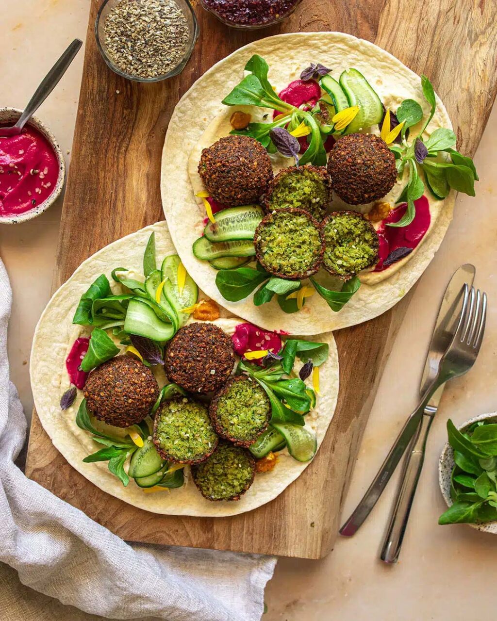 Zwei Wraps auf einem rustikalen Holzbrett, gefüllt mit selbstgemachten grünen Falafelbällchen, Rote Bete Hummus, frischem Salat und knackiger Gurke. Veredelt mit dem Bio Salat & Bowl Food Finisher Gewürz-Mix von Luis Dias für eine harmonische Würze.