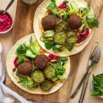 Zwei Wraps auf einem rustikalen Holzbrett, gefüllt mit selbstgemachten grünen Falafelbällchen, Rote Bete Hummus, frischem Salat und knackiger Gurke. Veredelt mit dem Bio Salat & Bowl Food Finisher Gewürz-Mix von Luis Dias für eine harmonische Würze.