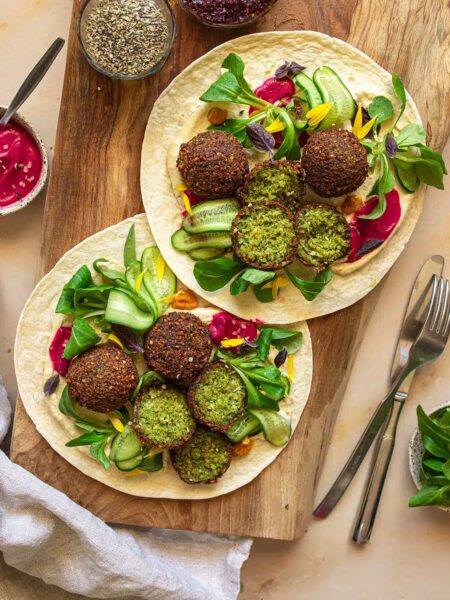 Zwei Wraps auf einem rustikalen Holzbrett, gefüllt mit selbstgemachten grünen Falafelbällchen, Rote Bete Hummus, frischem Salat und knackiger Gurke. Veredelt mit dem Bio Salat & Bowl Food Finisher Gewürz-Mix von Luis Dias für eine harmonische Würze.
