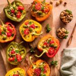 Gefüllte Grillpaprika auf einem Holzbrett, zubereitet nach einem Rezept von Sternekoch Luis Dias aus Köln. Die Paprika sind appetitlich angerichtet und mit einer würzigen Füllung gefüllt, die am oberen Rand der Paprika sichtbar ist. Das Bild zeigt eine Nahaufnahme der Paprika, die eine kräftige, goldbraune Farbe haben.