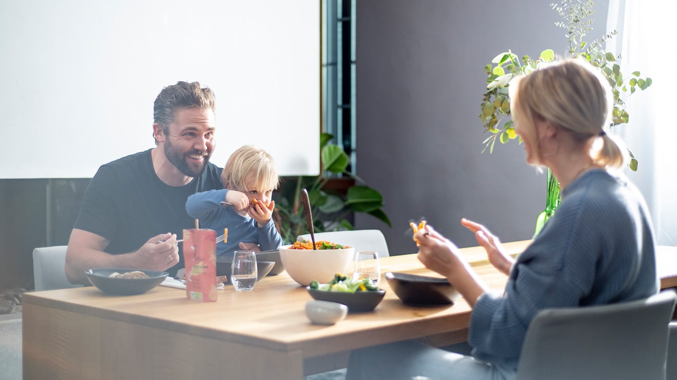Eine fröhliche Familie sitzt an einem Tisch während ihres Airbnb-Urlaubs. Die Eltern und das Kind lachen und genießen ihr Essen, das mit Bio Food Finisher Gewürzmischungen verfeinert wurde. Die Gewürzmischungen stehen auf dem Tisch, während die Familie die gemeinsame Mahlzeit in entspannter Atmosphäre genießt.