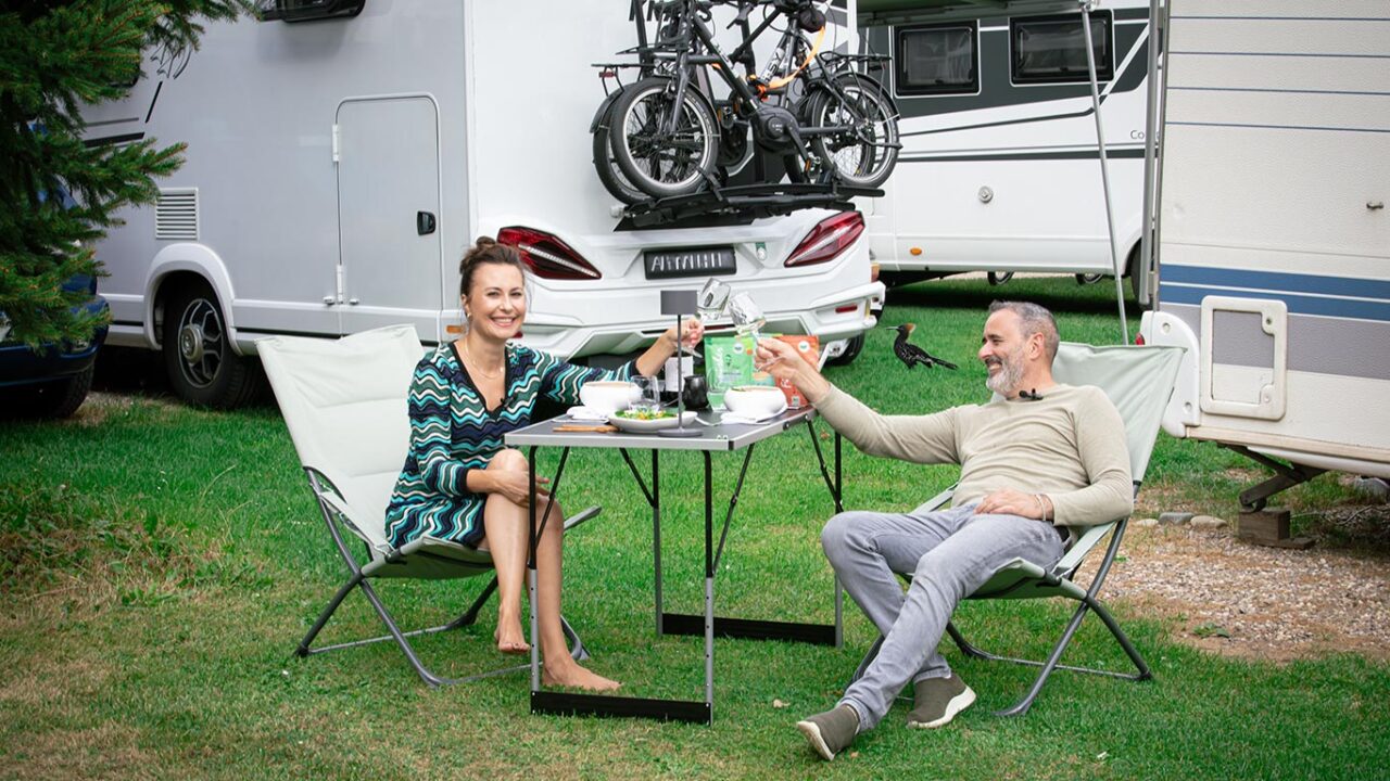 Ein Pärchen sitzt auf einem stilvoll eingedeckten Tisch auf einem Campingplatz und genießt ihr Essen in der Natur. Sie verwenden die fertige Gewürzzubereitung von Luis Dias, einem Sternekoch, die einfach über das fertige Gericht gestreut wird – die perfekte Gewürzlösung für Camping-Abenteuer.