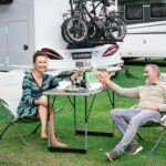 Ein Pärchen sitzt auf einem stilvoll eingedeckten Tisch auf einem Campingplatz und genießt ihr Essen in der Natur. Sie verwenden die fertige Gewürzzubereitung von Luis Dias, einem Sternekoch, die einfach über das fertige Gericht gestreut wird – die perfekte Gewürzlösung für Camping-Abenteuer.