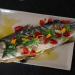 Ein perfekt zubereiteter Fischfilet, goldbraun gebraten und kunstvoll angerichtet, garniert mit frischen Kräutern und Zitronenscheiben, serviert auf einem eleganten Teller.