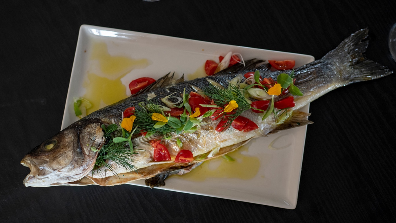 Ein perfekt zubereiteter Fischfilet, goldbraun gebraten und kunstvoll angerichtet, garniert mit frischen Kräutern und Zitronenscheiben, serviert auf einem eleganten Teller.