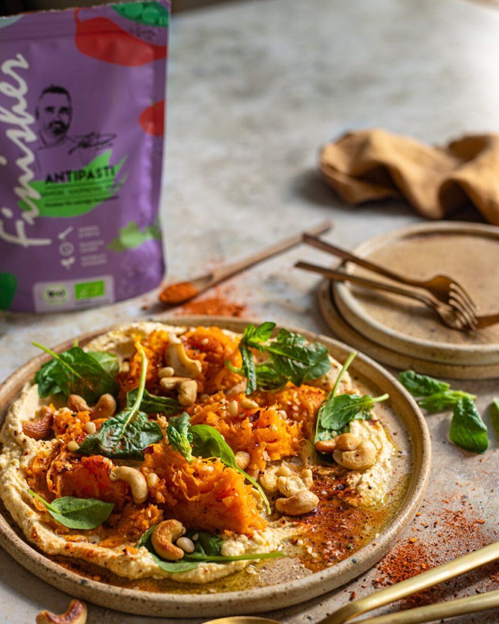 Herbstliches Kürbisgericht auf Hummus, garniert mit Cashewkernen, Spinat und mediterranen Gewürzen, verfeinert mit Bio Antipasti Food Finisher.