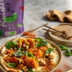 Herbstliches Kürbisgericht auf Hummus, garniert mit Cashewkernen, Spinat und mediterranen Gewürzen, verfeinert mit Bio Antipasti Food Finisher.