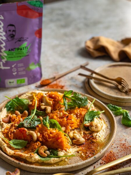 Herbstliches Kürbisgericht auf Hummus, garniert mit Cashewkernen, Spinat und mediterranen Gewürzen, verfeinert mit Bio Antipasti Food Finisher.
