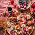 Ein Teller mit frisch gebackenen, Vegane Pancakes verfeinert mit Bio Porridge Food Finisher. Die Pfannkuchen sind locker und fluffig, garniert mit der aromatischen Bio- und veganen Gewürzzubereitung, die aus hochwertigem Hibiskusblüten*, Orangenschalen*, Mangopulver*, getrocknete, gemahlene Datteln*, Tonkabohne* besteht. Ein köstliches Frühstück oder Dessert, das sowohl optisch als auch geschmacklich überzeugt. Das Bild stammt aus einem Rezept von Luis Dias, einem Spitzenkoch.