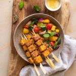 Bunte Gemüse-Grillspieße aus Mais, roter und gelber Paprika, Zucchini, Radieschen und roten Zwiebeln, perfekt gewürzt mit einer Bio Mediterran Food Finisher Gewürzmischung, die als erstes auf das fertige Gericht gestreut wird. Die Spieße sind kunstvoll arrangiert und werden auf einem rustikalen Holzbrett serviert, bereit zum Genießen.