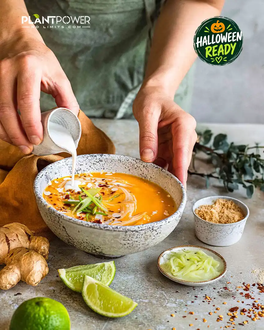 Halloween-Rezept: Kokosmilch wird in asiatische Kürbissuppe gegossen, daneben liegen Ingwer und Limetten.