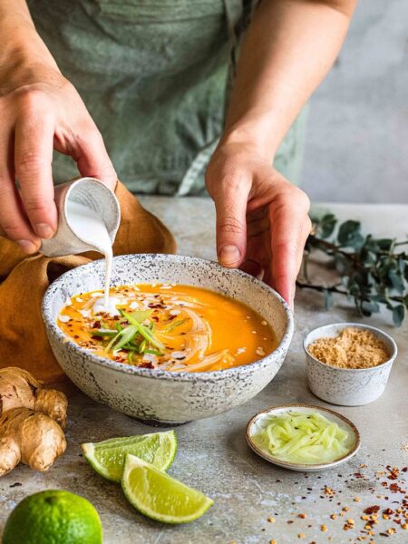 Ein Teller mit cremiger asiatischer Kürbissuppe, garniert mit frischen Kräutern und Kürbiskernen, auf einem rustikalen Holztisch.