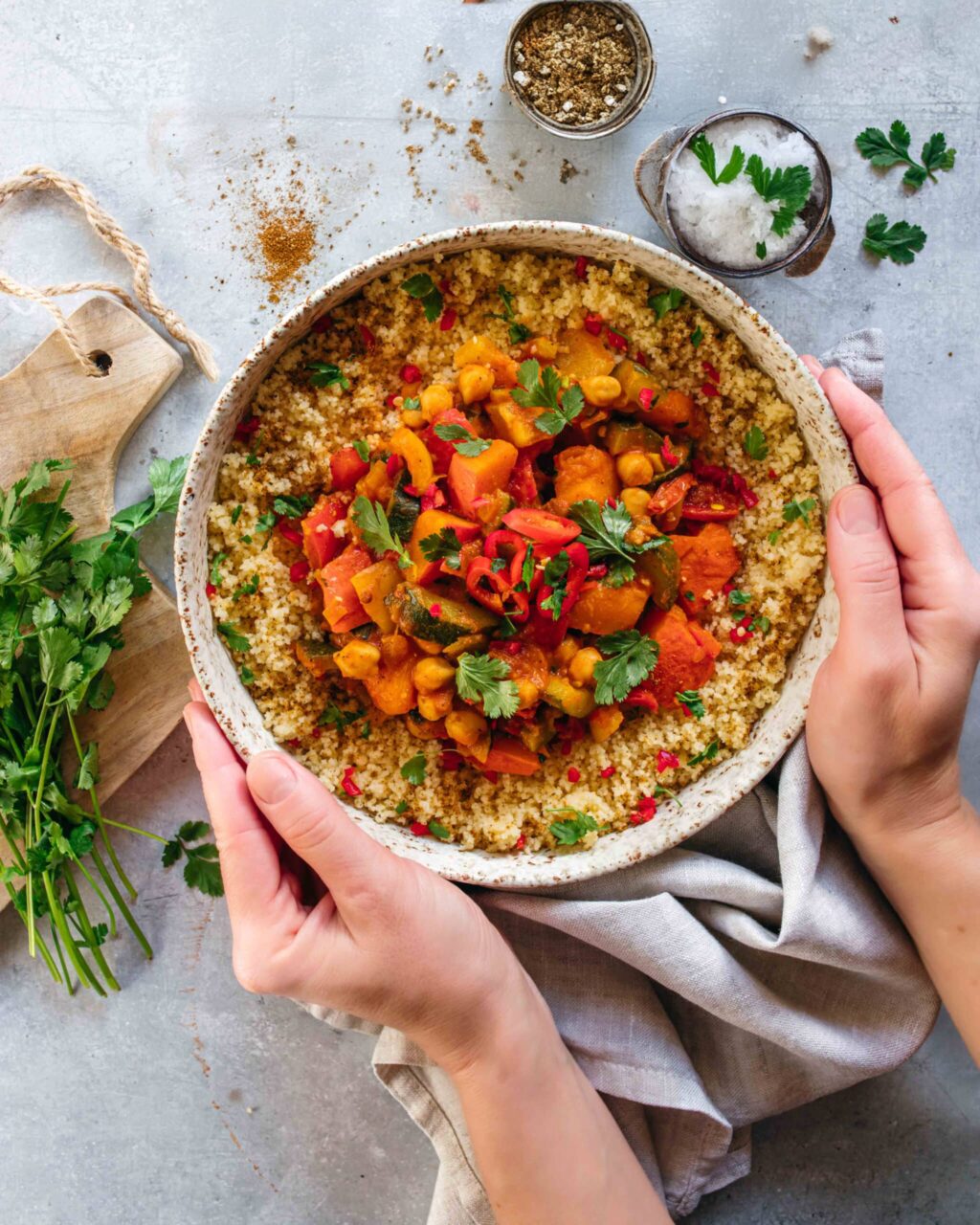 Ein Teller mit aromatischem Gemüse-Couscous, garniert mit frischen Kräutern, serviert in einer rustikalen Schale, die von zwei Händen gehalten wird. Das Gericht strahlt Wärme und Frische aus – perfekt für ein leichtes und köstliches Essen.