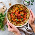 Ein Teller mit aromatischem Gemüse-Couscous, garniert mit frischen Kräutern, serviert in einer rustikalen Schale, die von zwei Händen gehalten wird. Das Gericht strahlt Wärme und Frische aus – perfekt für ein leichtes und köstliches Essen.