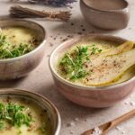 Geröstete Pastinaken-Birnen-Suppe mit frischer Kresse, Birnenscheiben und Pfeffer, serviert in rustikalen Keramikschalen, dekoriert mit Lavendel und Meersalz.