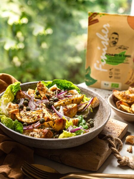 Frischer Salat mit goldbraun gerösteten Kartoffelecken, roten Zwiebeln, Kapern und Gewürzen von Food Finisher Spices vor einer grünen Naturkulisse.