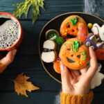 Frau hält eine Tasse Kaffee in der einen und bunte Halloween Cookies in der anderen Hand. Im Hintergrund herbstliche Deko mit Kürbis, Blättern und Food Finisher Spices. Perfekt für herbstliche Backideen und Halloween-Rezepte mit Bio-Gewürzen. 100 % Bio, vegan, ohne Zusatzstoffe.