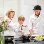Eine Familie kocht gemeinsam in der Küche, während verschiedene Gewürze auf der Arbeitsfläche stehen. Ein inspirierender Moment für Kochanfänger, um mit Gewürztipps und Tricks den Einstieg in die Küche zu finden.