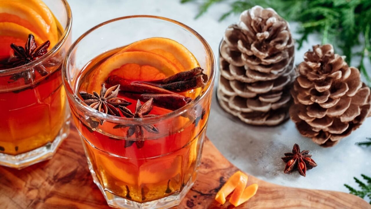 Winterliches Bild mit dampfendem Glühwein im Glas, Tannenzapfen, Zimtstangen und winterlichen Gewürzen. Symbolisiert die aromatische Gewürzvielfalt im Winter mit Food Finisher Spices. Bio-zertifizierte Gewürzmischungen, vegan, ohne Zusatzstoffe.