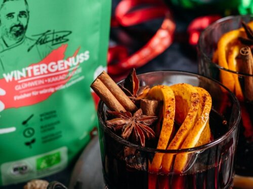Zwei dampfende Glühwein-Gläser, dekoriert mit Zimtstangen und Orangenscheiben. Im Hintergrund sichtbar: Wintergenuss Food Finisher Spices. Aromatische Bio-Gewürzmischung mit Zimt, Hibiskus, Datteln und Tonkabohne. 100 % Bio, vegan, ohne Zusatzstoffe, ideal für die Winterzeit.