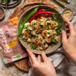 Ein Teller mit geröstetem Blumenkohl, dekoriert mit roten und grünen Peperoni. Daneben liegt eine Packung des Bio Go Wild Food Finisher von Food Finisher Spices.