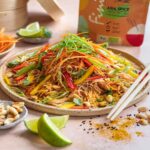 Ein Teller mit asiatischem Krautsalat, verziert mit Gemüsestreifen und Limettenstücken, begleitet von einer Packung Bio Asia Food Finisher im Hintergrund.