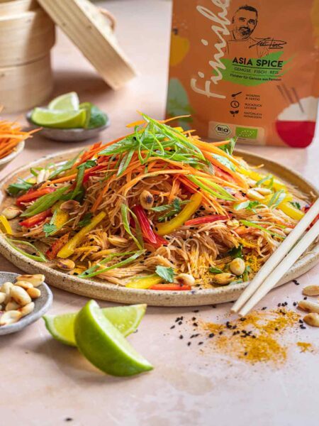 Ein Teller mit asiatischem Krautsalat, verziert mit Gemüsestreifen und Limettenstücken, begleitet von einer Packung Bio Asia Food Finisher im Hintergrund.