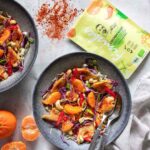 Ein köstlicher Hähnchensalat mit Mandarinen, Rotkohl, Paprika und Erdnüssen, serviert in einer grauen Schüssel, begleitet von einer Bio Asia Food Finisher-Verpackung.