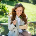 Eine Frau sitzt entspannt im Park und genießt einen frischen, gesunden Salat. Die grüne Natur um sie herum unterstreicht ihren bewussten Lebensstil und ihre gesunde Ernährung.