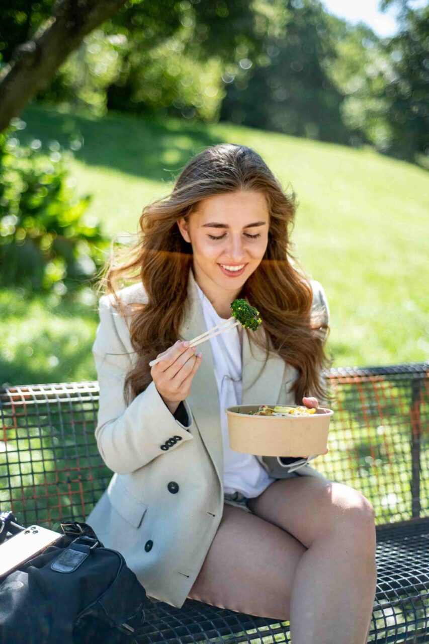 Eine Frau sitzt entspannt im Park und genießt einen frischen, gesunden Salat. Die grüne Natur um sie herum unterstreicht ihren bewussten Lebensstil und ihre gesunde Ernährung.